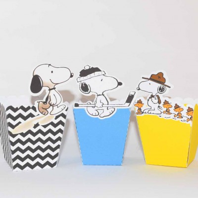 Caixas de festa decorativas com personagens Snoopy em preto e branco, azul e amarelo.