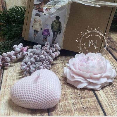 Velas decorativas rosa em formato de coração e flor sobre mesa de madeira com caixa ao fundo