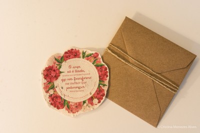 cartão floral redondo com texto em português e envelope castanho amarrado com cordão