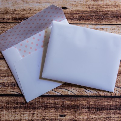 Envelope branco com padrão de bolinhas cor-de-rosa no interior e cartão branco sobre madeira