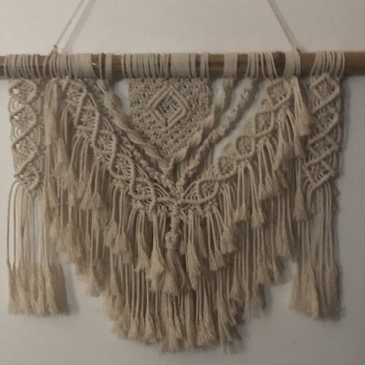 Decoração de parede em macramé bege com franjas e padrões trançados