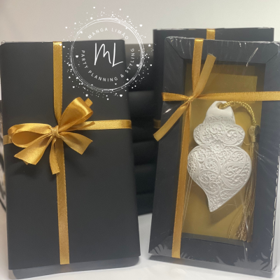 Pacotes pretos com fita dourada e ornamento branco decorativo em embalagem transparente.