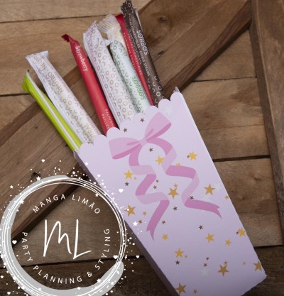 Pacotes coloridos de palhinhas em caixa rosa com laço e estrelas douradas sobre madeira