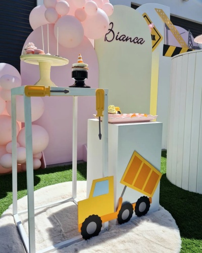 Expositor branco com cupcakes e decorações de construção e balões cor-de-rosa