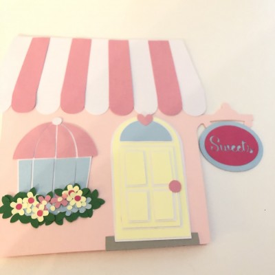 Ilustração colorida de fachada de loja cor-de-rosa com tenda, porta, janela e placa 'Sweets'