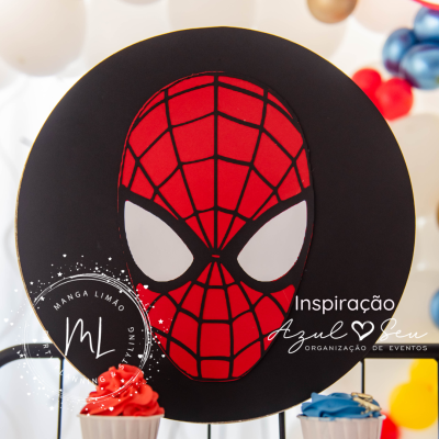 Adorno com máscara do Homem-Aranha vermelho e preto, cupcakes coloridos e balões ao fundo.