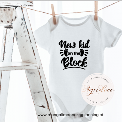 Body de bebé branco com texto em preto pendurado numa corda ao lado de banco rústico branco