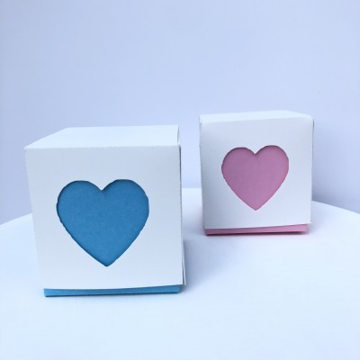 Dois cubos de papel branco com corações recortados em azul e rosa.