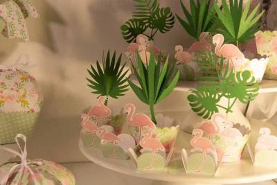 Doces decorados com folhas verdes e flamingos cor-de-rosa sobre suportes brancos.