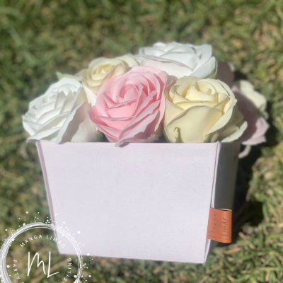 Caixa cor-de-rosa claro com flores artificiais de espuma em branco, creme e rosa aberta sobre relva