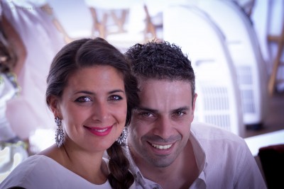 Casal sorridente em ambiente interior com cadeira e planta ao fundo