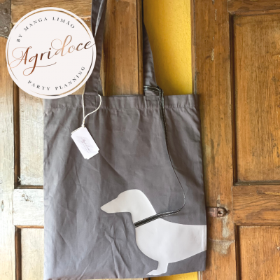 Saco de tecido cinzento com impressão de cão branco pendurado em porta de madeira.