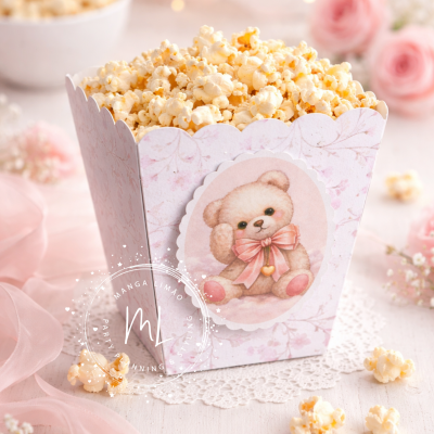 Caixa rosa com ursinho e pipocas sobre superfície clara com rosas.