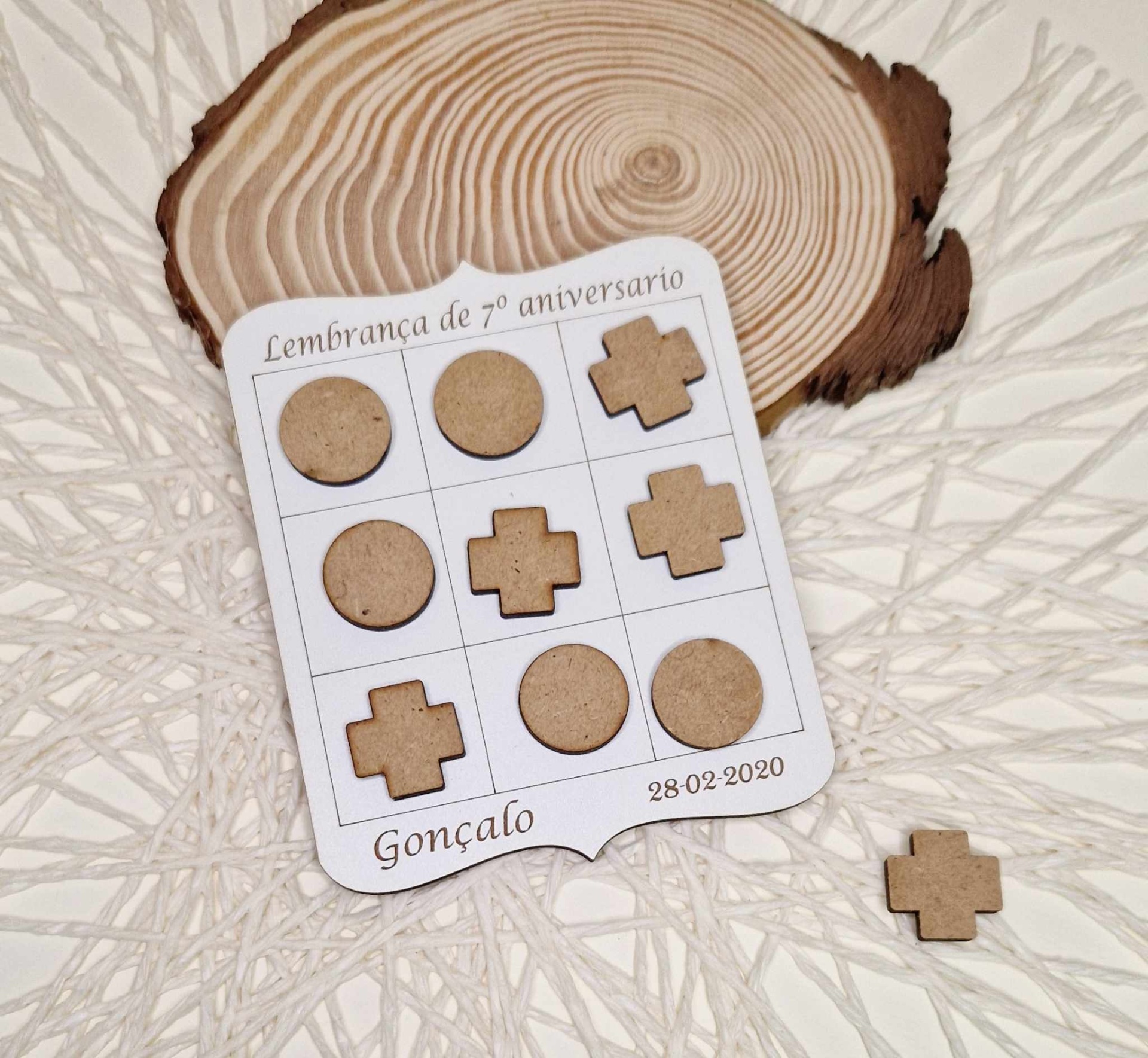 Jogo do Galo Personalizado Jogo de peças de madeira redondas e em cruz sobre cartão branco comemorativo e base decorativa clara com padrão texturizado.