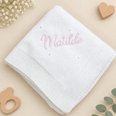 Manta branca com bordado rosa do nome Matilde, enfeites de madeira e folhas verdes