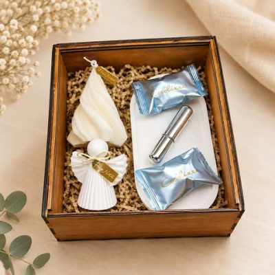 Conjunto presente com velas natalinas, doces e objeto metálico numa caixa de madeira