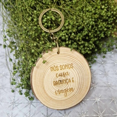 Chaveiro de madeira com texto gravado e planta verde ao fundo