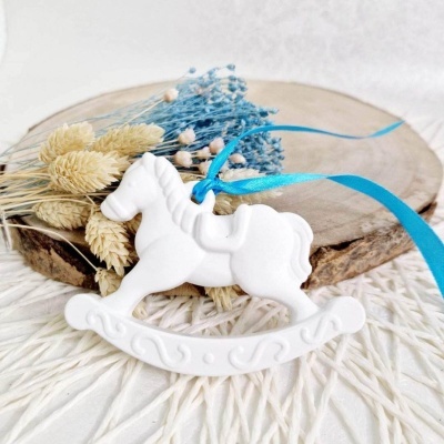 Ornamento cavalo de balanço branco com fita azul e flores secas sobre base de madeira