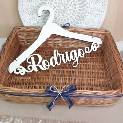 Cabide branco com nome Rodrigo dentro de cesta de vime com laço azul