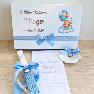 Conjunto de batismo com cartão, vela, concha e toalha decorados com fitas e texto comemorativo.