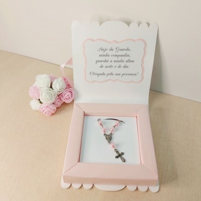 Convite rosa com terço e texto em português, ao lado de flores cor-de-rosa e brancas