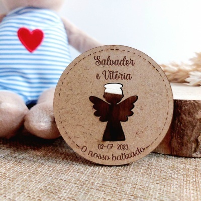 Placa redonda de madeira clara com anjo em madeira escura e texto de batizado em português