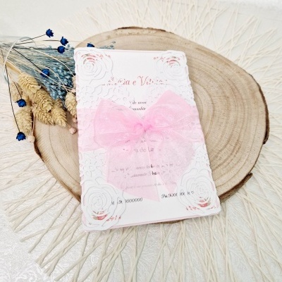 Convite branco com laço rosa sobre base de madeira com flores secas