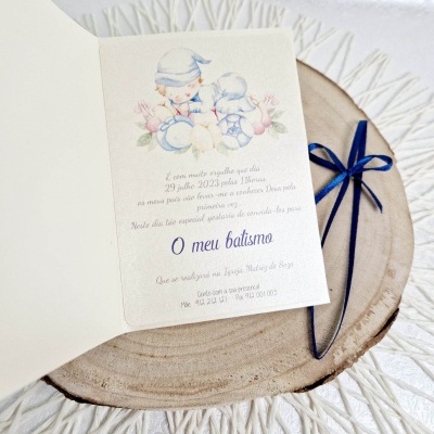 Convite de batismo aberto com ilustração de crianças e texto em português sobre base de madeira redonda