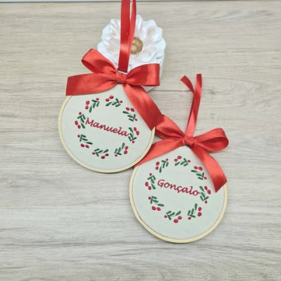 Dois enfeites redondos bordados com nomes Manuela e Gonçalo com laços vermelhos