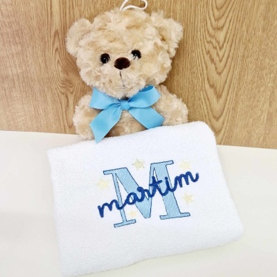 Ursinho de pelúcia castanho com laço azul e toalha branca bordada com o nome Martim