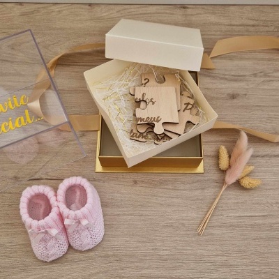 Caixa com puzzle de madeira, sapatinhos de bebé cor de rosa e flores secas sobre madeira clara