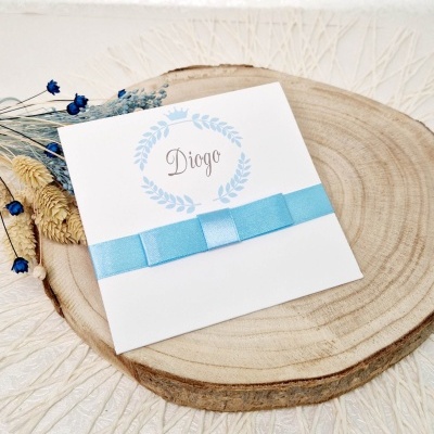 Convite branco com laço azul e texto 'Diogo' sobre um disco de madeira