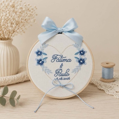 Bastidor com bordado de flores azuis, nomes Fátima & Paulo e data 15.08.2026 com fita azul