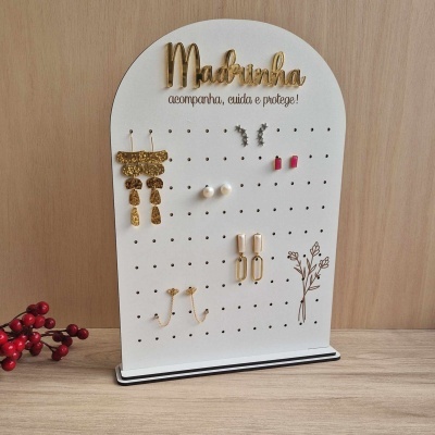 Expositor branco de brincos com texto 'Madrinha' e flores, vários brincos pendurados
