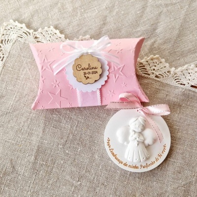 Embalagem rosa com textura de estrelas e medalha branca com anjo e texto em português.
