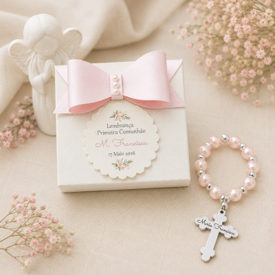Caixa branca com laço rosa e etiqueta para primeira comunhão e pulseira rosa com cruz prateada.