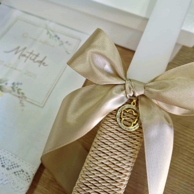 Vela decorativa bege com fita de cetim e pendente dourado junto a envelope branco com texto Matilde