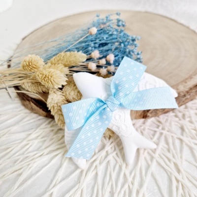 Estrela de cerâmica branca com laço azul e raminhos secos em fundo branco e madeira