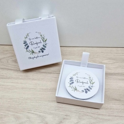 Espelho compacto branco com design floral e texto comemorativo em caixa branca.