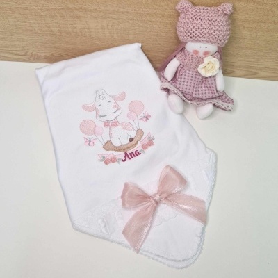 Fralda branca bordada com girafa e nome Ana, com laço rosa, e boneca de crochet rosa com vestido xadrez