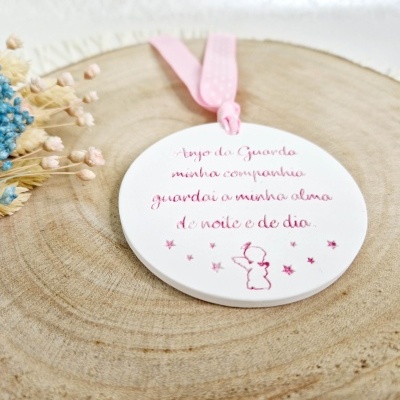 Placa branca redonda com cordão rosa e texto em português sobre tronco de madeira