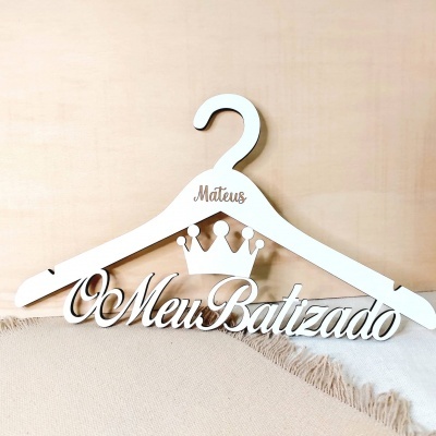 Cabide branco em madeira com texto personalizado e coroa decorativa sobre tecido bege