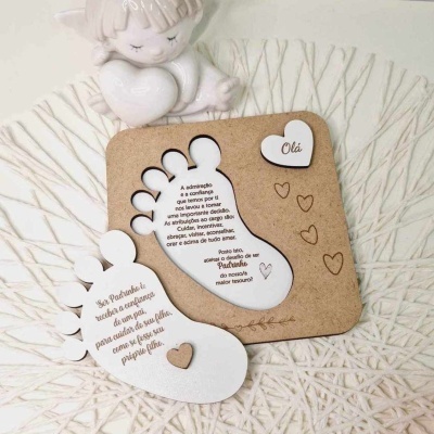 Suportes em formato de pés com texto em português, base castanha, sobre superfície branca trançada e anjo decorativo branco ao fundo