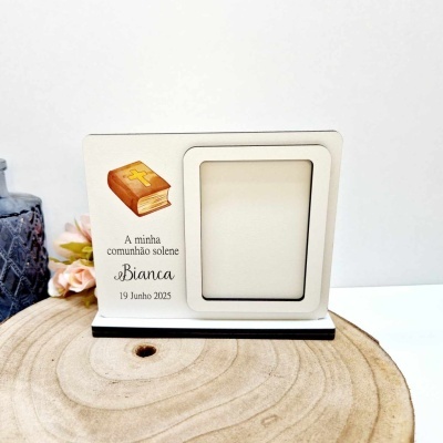 Moldura branca com base preta e decoração de comunhão solene ao lado de flores e vaso azul