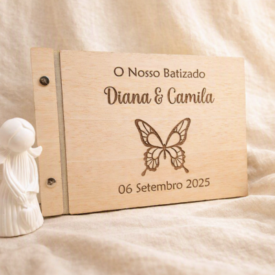 Livro de memórias em madeira clara gravado para batizado com texto e borboleta ao lado de figura decorativa branca