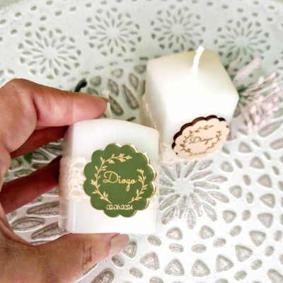 Duas velas brancas quadradas com etiquetas personalizadas e mesa branca com padrão recortado