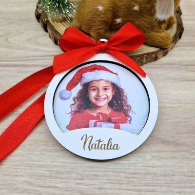 Ornamento redondo branco com foto de menina com gorro de Natal e texto Natalia