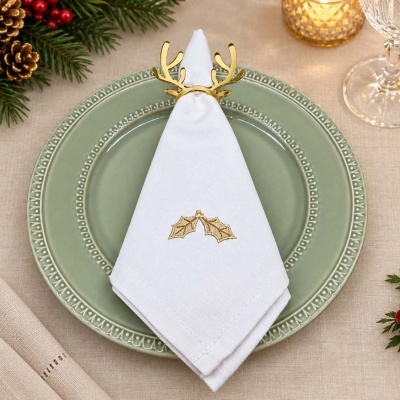 Guardanapo branco com bordado dourado e argola de chifres em prato verde numa mesa decorada