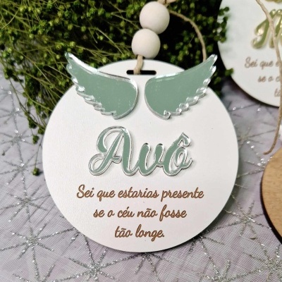 Placa decorativa branca redonda com asas verdes e texto em português, pendurada por fio com contas