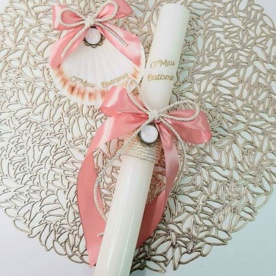 vela e concha decoradas com fita rosa e cordão bege sobre suporte dourado com padrão de folhas
